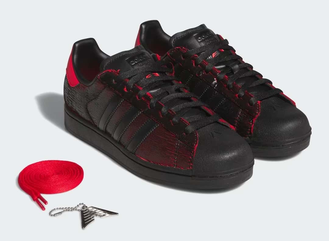 Par de adidas Superstar Halloween de Anthony Edwards sobre fondo gris claro, junto a un par de cordones rojos de repuesto y un dije metálico