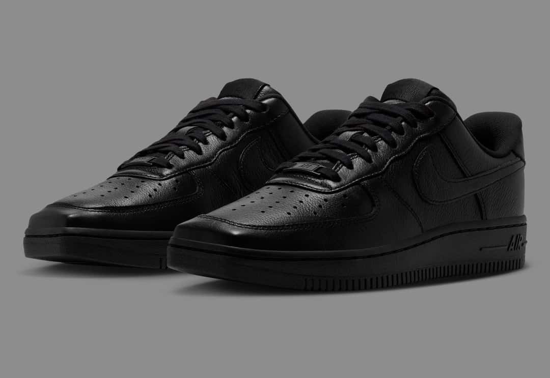 Par de Nike Air Force 1 Low de punta cuadrada Triple Black sobre fondo gris, todo de cuero negro con la puntera cuadrada