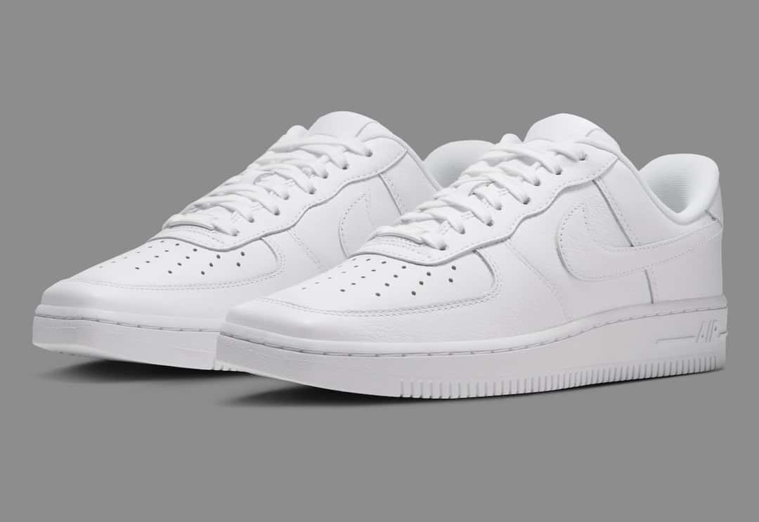 Par de Nike Air Force 1 Low de punta cuadrada Triple White sobre fondo gris, con la puntera alargada y plana