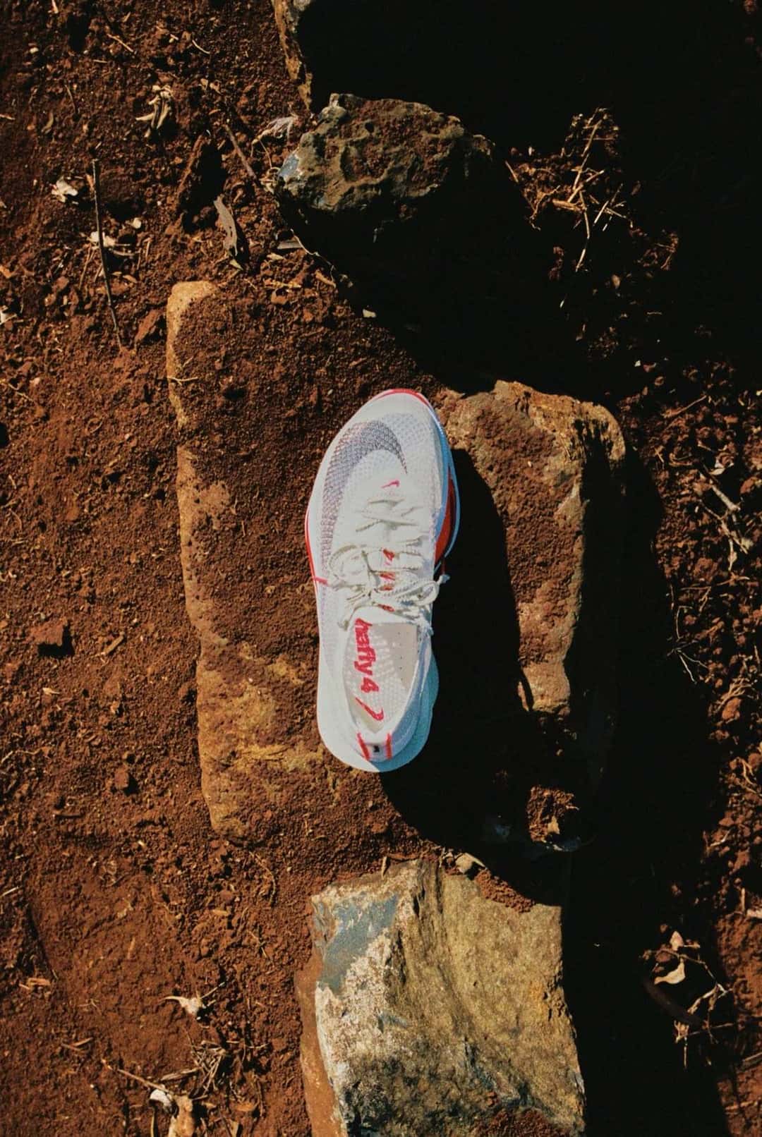 Nike Alphafly 4 blanca con detalles rojos apoyada sobre una piedra en un camino de tierra, vista desde arriba