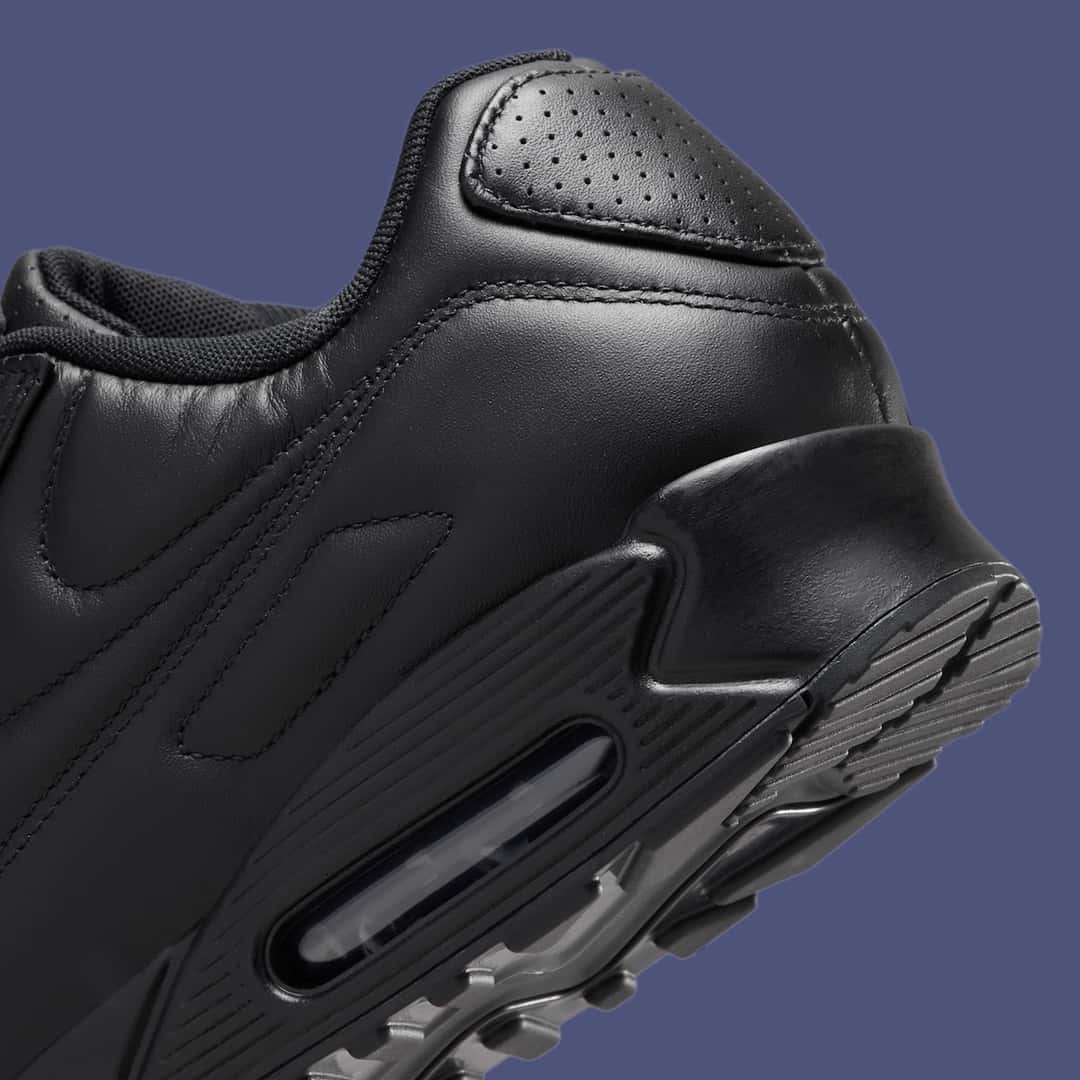 Detalle del talón de la Nike Air Max 90 SP Black Leather sobre fondo azul grisáceo, con cuero negro perforado en la zona del talón y la cámara Air visible en la suela