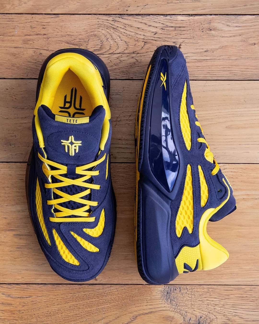 Par de Reebok Engine A 26 Brew Crew sobre un piso de madera, visto desde arriba, con la plantilla amarilla y el logo cruzado de Nate Ament en la lengüeta