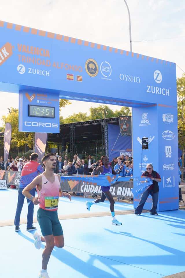 Sheila Chepkirui, de musculosa violeta, corta la cinta de llegada del Medio Maratón de Valencia con 1:03:51 en el reloj; adelante pasa un corredor de musculosa rosa