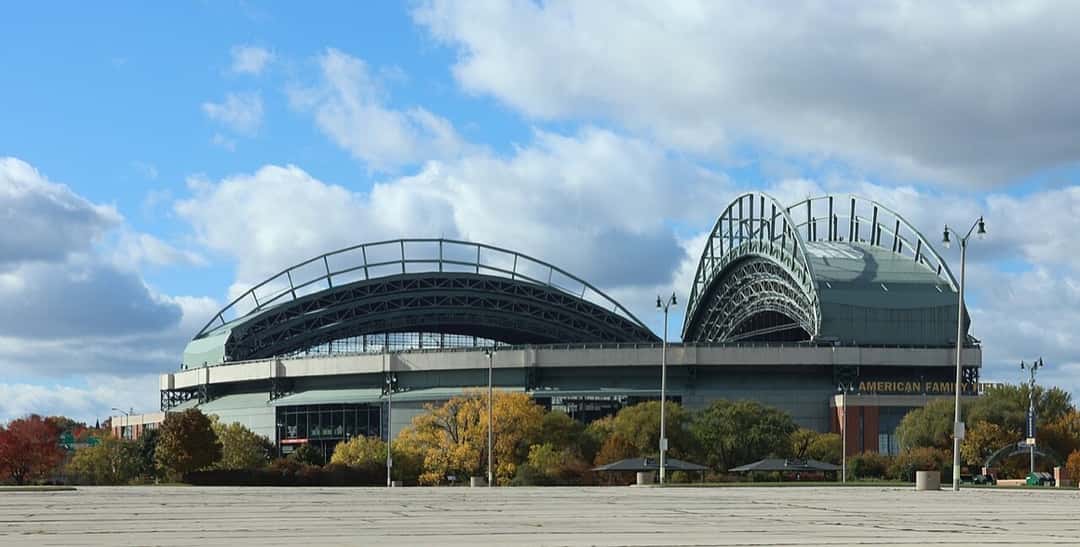Imagen del estadio: el American Family Field de Milwaukee, con su techo de arcos metálicos, rodeado de árboles en otoño