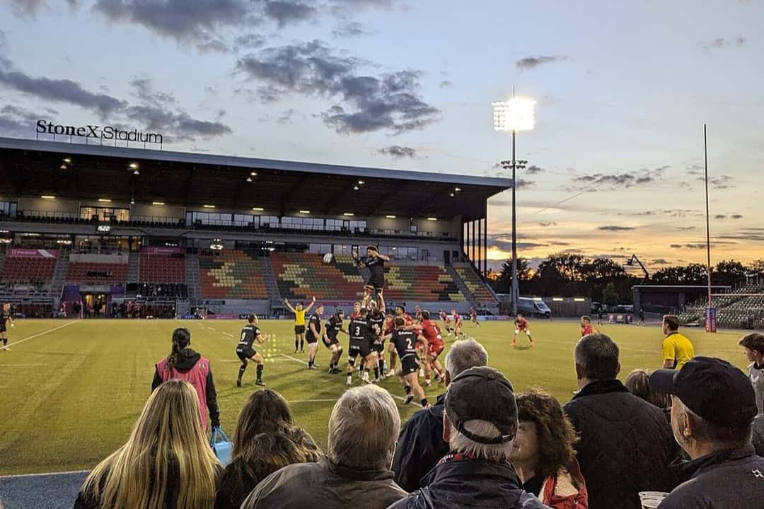 Foto de archivo: un line de Saracens, de negro, ante Scarlets en el StoneX Stadium al atardecer, con el público en primer plano