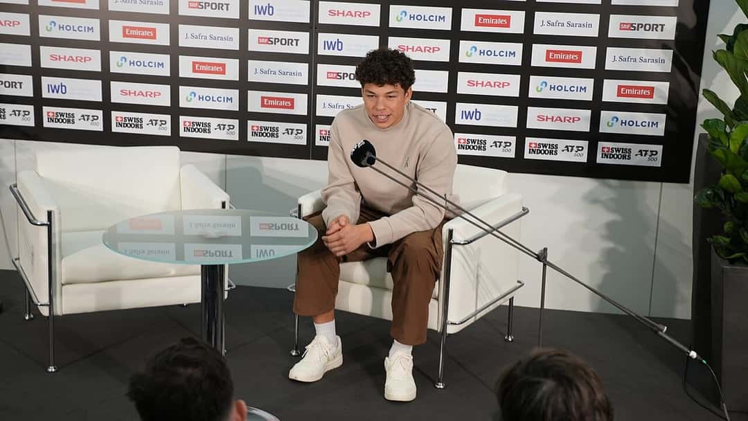 Foto de archivo: Ben Shelton, con buzo claro, habla en la conferencia de prensa del Swiss Indoors de Basilea, sentado en un sillón blanco frente a un panel de sponsors