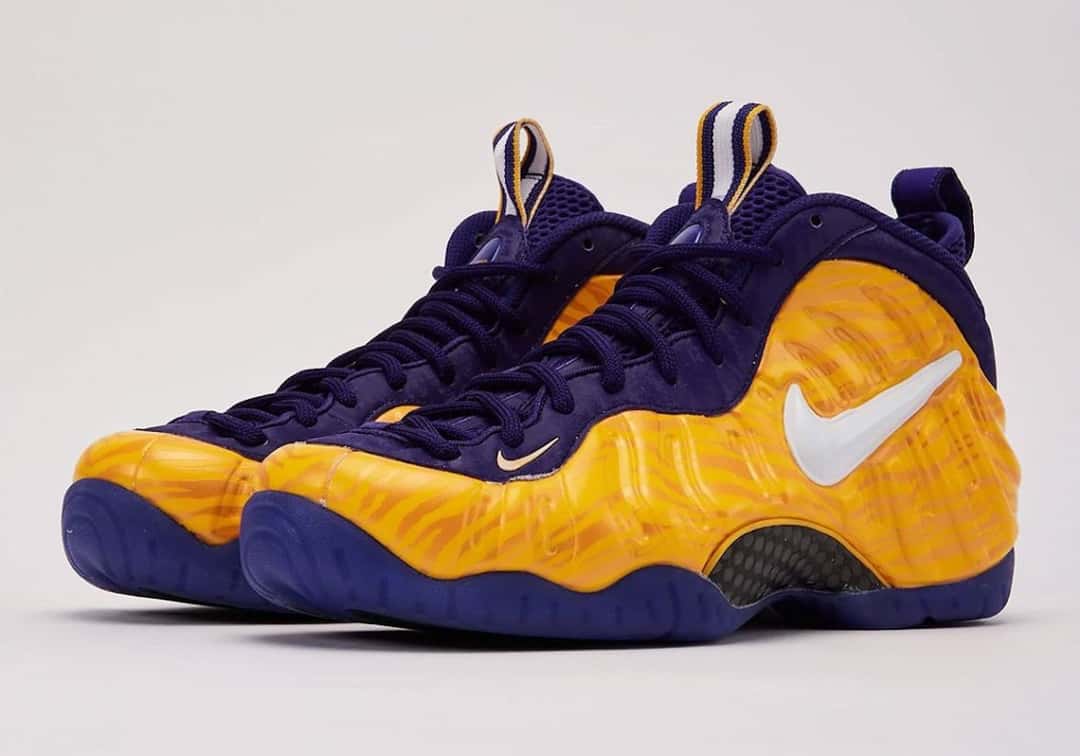 Par de Nike Air Foamposite Pro LSU en amarillo con cuello y suela violeta y Swoosh blanco, sobre fondo gris claro