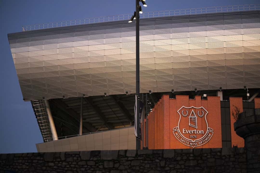 El Hill Dickinson Stadium, la nueva cancha del Everton, con su fachada metálica iluminada al atardecer y el escudo del club sobre una pared de ladrillo; foto de archivo (foto: prensa Everton FC)