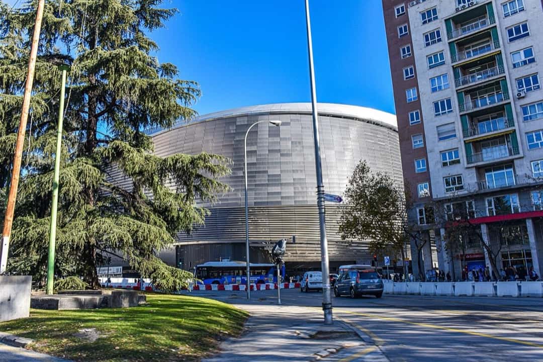 El exterior del estadio Santiago Bernabéu de Madrid, con su nuevo revestimiento metálico plateado, visto desde una calle con árboles y edificios; foto de archivo de diciembre de 2024 (foto: MottaW, Wikimedia Commons, licencia CC BY 4.0)