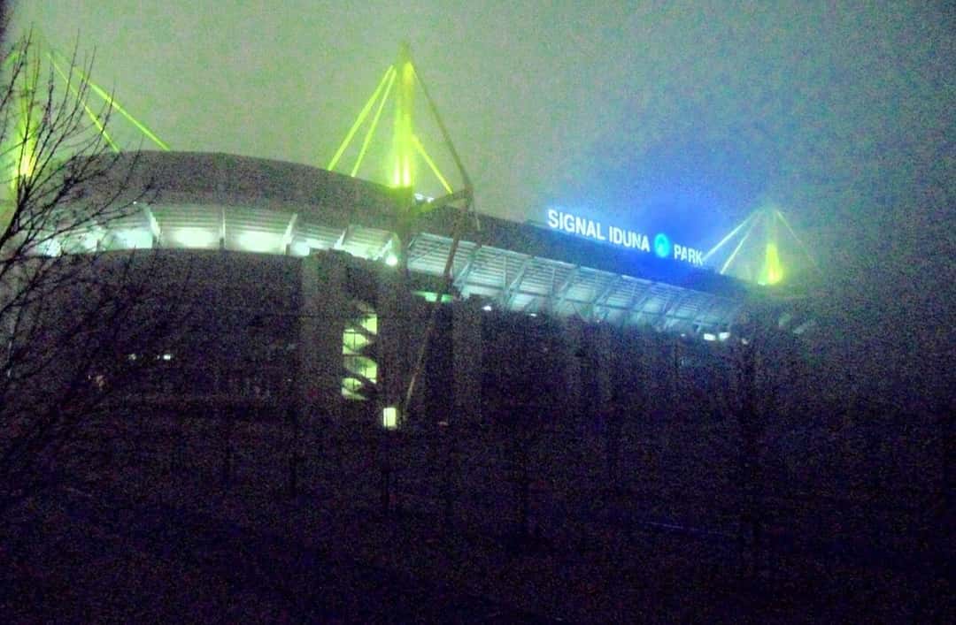El Signal Iduna Park de noche, con las torres iluminadas y el cartel del estadio en la fachada; foto de archivo (foto: Matthias Nonnenmacher, Wikimedia Commons, licencia CC BY-SA 4.0)