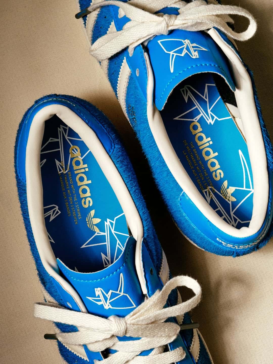 Vista desde arriba de las plantillas azules de la adidas Superstar de Liberaiders, con grullas de origami en blanco, el logo adidas en dorado y la grulla bordada en la lengüeta