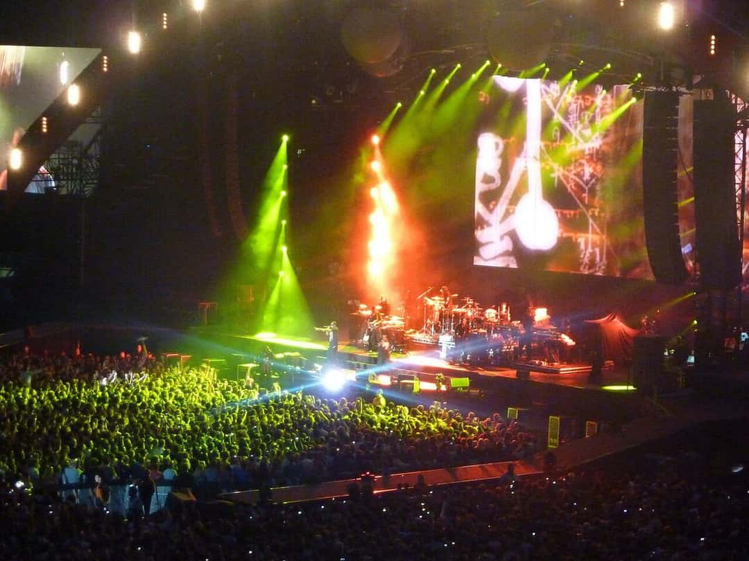 Jay-Z sobre un escenario lleno de luces verdes y naranjas, frente a una multitud y con su banda atrás, en un show de 2009 (foto de archivo). Foto: wonker, CC BY 2.0, vía Wikimedia Commons