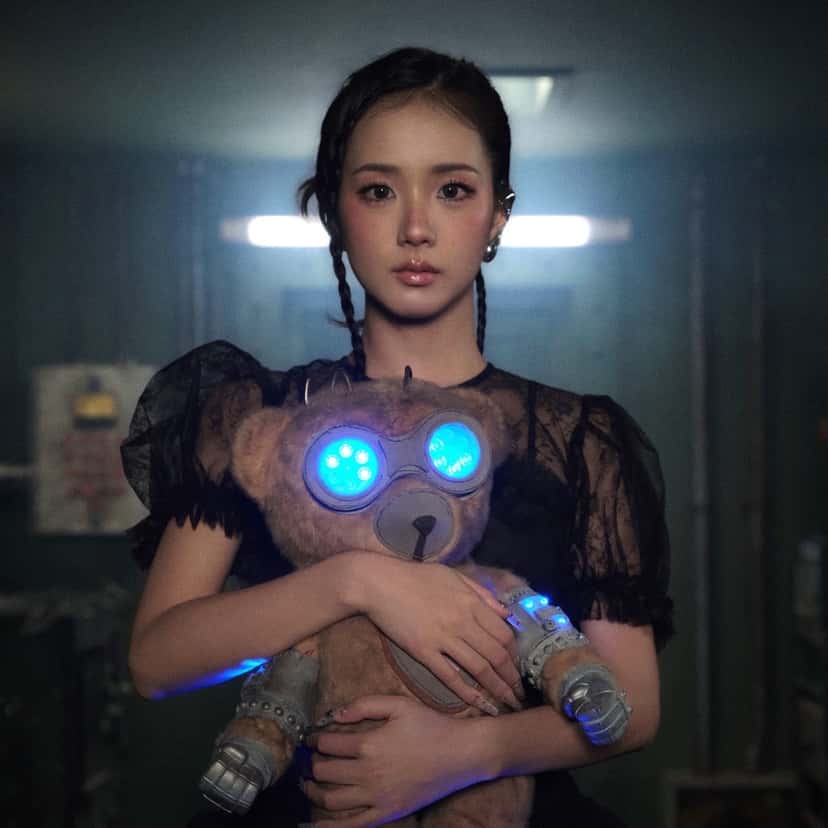 Portada del single «CLICK», de Jisoo: la cantante, con dos trenzas y vestido negro, abraza un oso de peluche con anteojos luminosos celestes en un pasillo oscuro