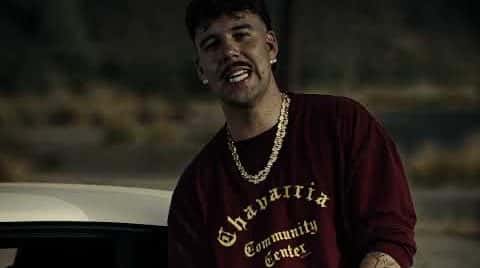 Fotograma del video oficial de «DOGGY»: un cantante con buzo bordó con letras doradas y cadena gruesa, apoyado en un auto blanco en un descampado