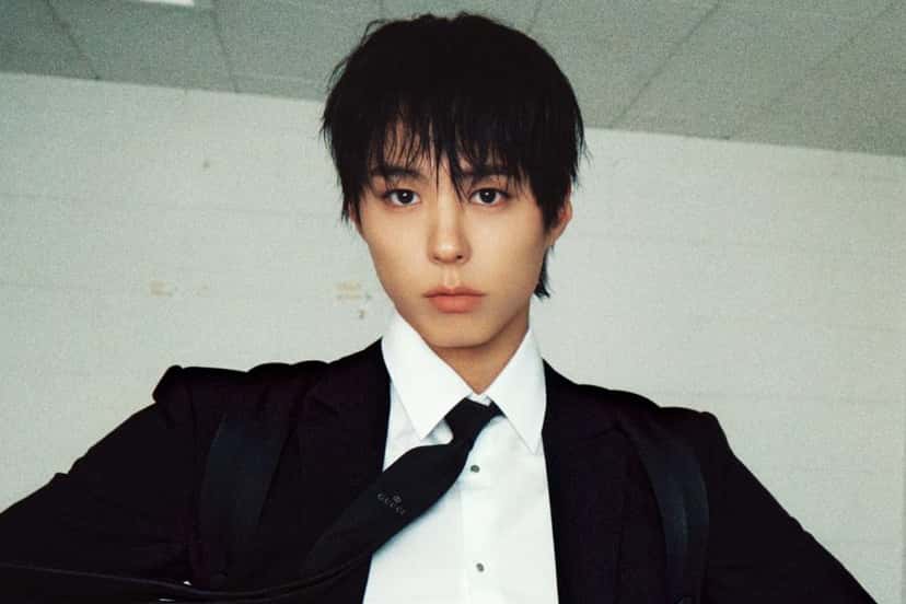 El actor Park Bo Gum, con el pelo negro sobre la frente, camisa blanca, corbata negra y saco oscuro, posa de frente contra una pared clara, en la foto de prensa oficial de los MAMA Awards 2026