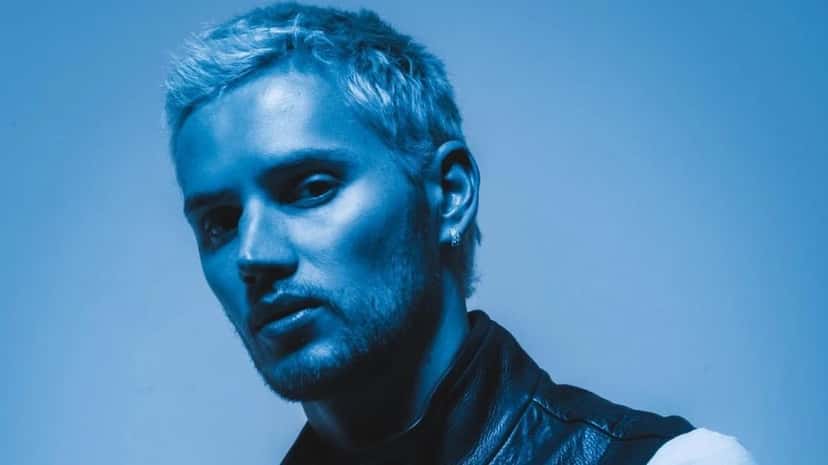 Foto de prensa de Mau P: retrato del DJ con el pelo rubio peinado hacia atrás y campera de cuero, iluminado con luz azul