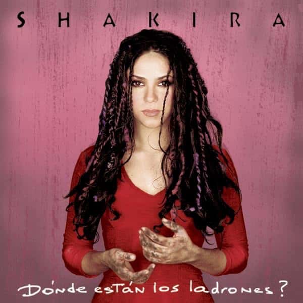 Portada de «¿Dónde están los ladrones?», de Shakira: la cantante, de vestido rojo y trenzas largas, con las manos juntas, sobre un fondo rosado