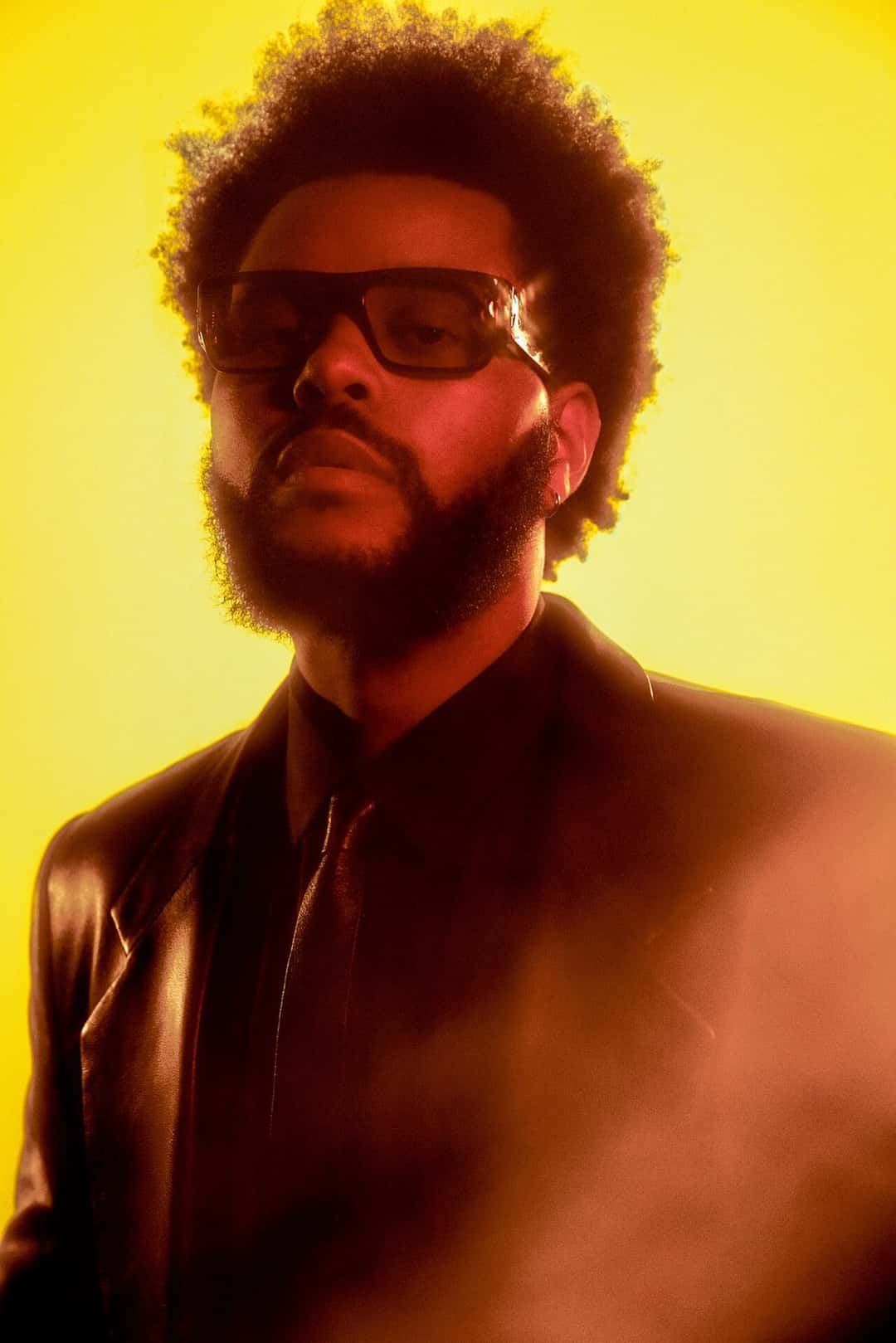 The Weeknd, con anteojos oscuros y saco negro, en una foto de prensa sobre fondo amarillo (foto de archivo). Foto: Brian Ziff, CC BY-SA 4.0, vía Wikimedia Commons