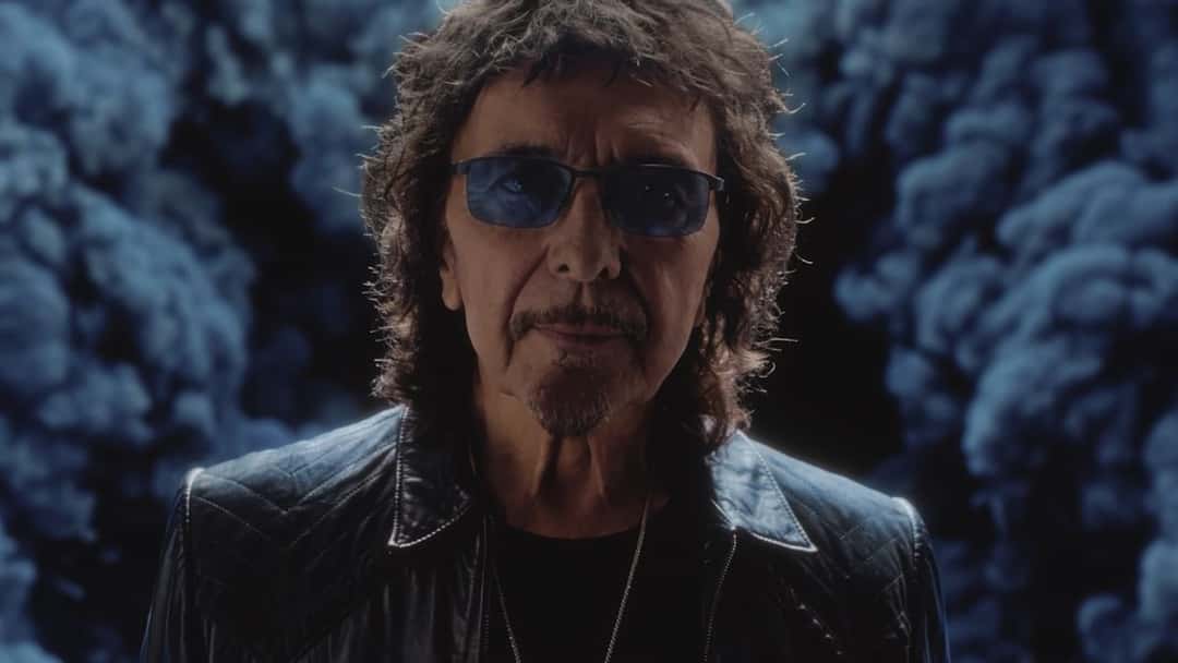 Fotograma del video oficial de «World Alone»: Tony Iommi, con anteojos de cristales azules y campera de cuero negra, mira a cámara delante de un humo azul oscuro