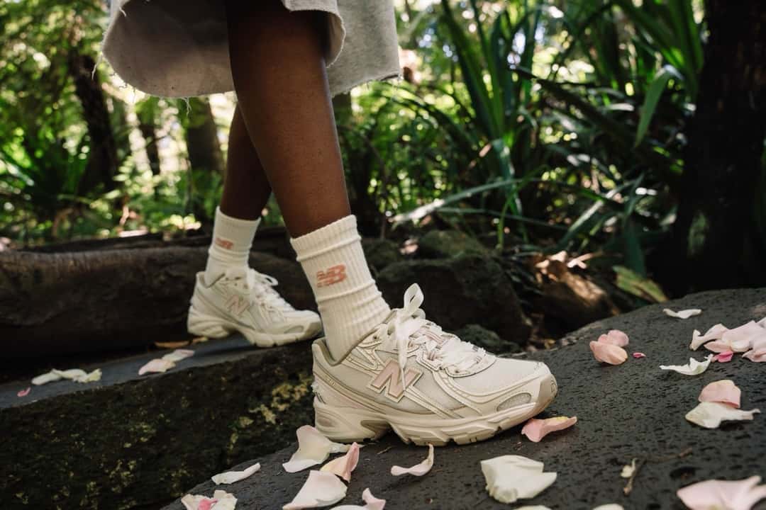 Piernas con medias blancas y zapatillas New Balance del Sakura Pack en marfil, sobre una piedra rodeada de pétalos