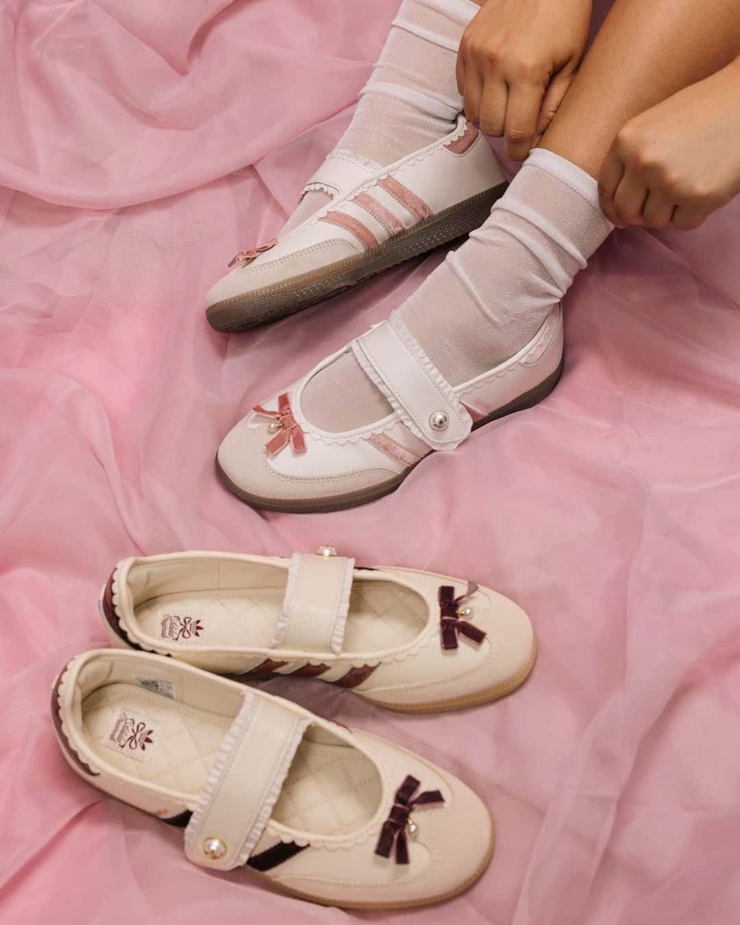 Dos pares de adidas Samba Jane Bow sobre tela rosa, uno rosa puesto con medias blancas y otro bordó