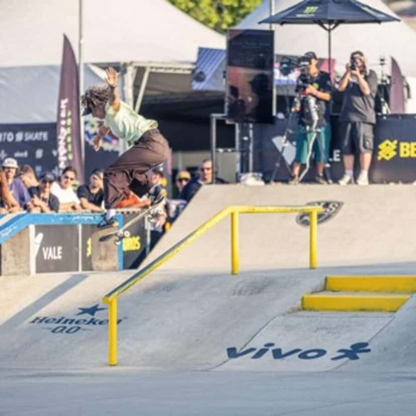 Un skater salta sobre una baranda amarilla en una pista de street, frente al público y a dos camarógrafos (foto de archivo)