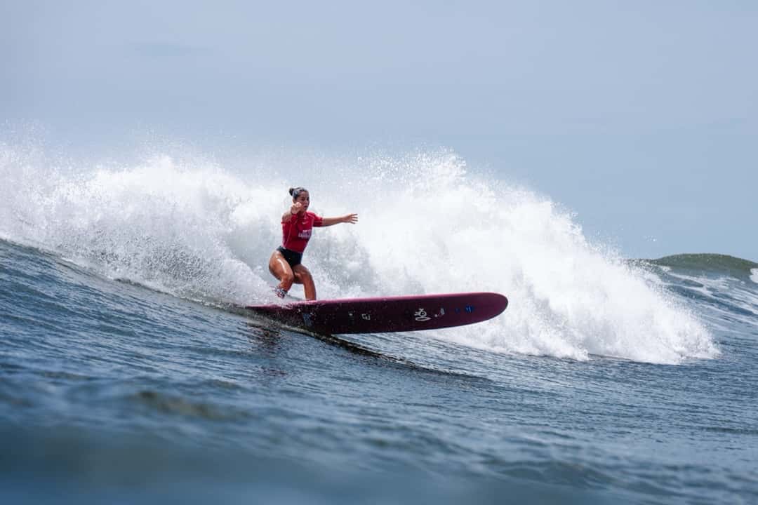 Lia Diaz, con lycra roja, gira con su longboard bordó sobre una ola de El Sunzal con la espuma detrás