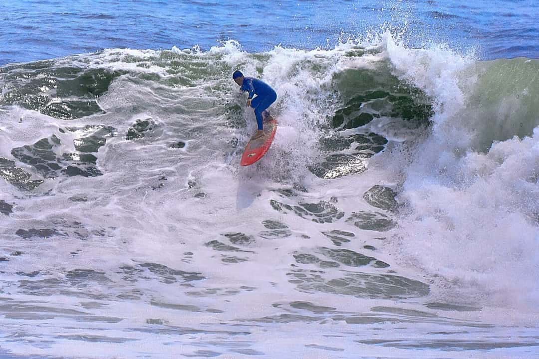 Un surfista con traje azul y tabla roja baja una ola espumosa de Punta Rocas, al sur de Lima (foto de archivo)