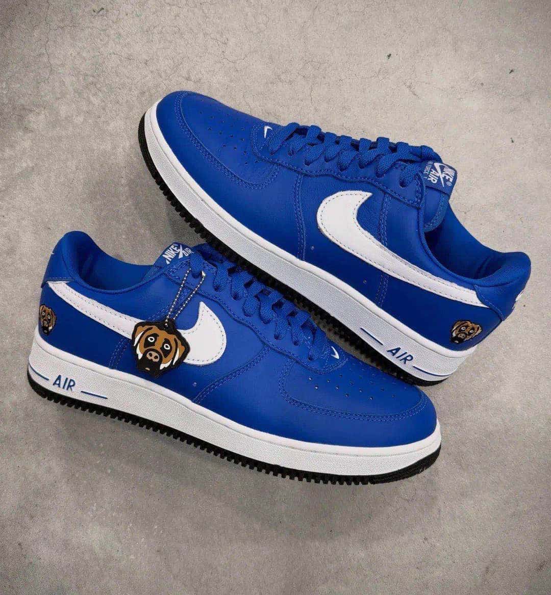 Par de Nike Air Force 1 '01 de Victor Victor en azul apoyado sobre un piso de cemento, con el llavero del perro colgando de los cordones