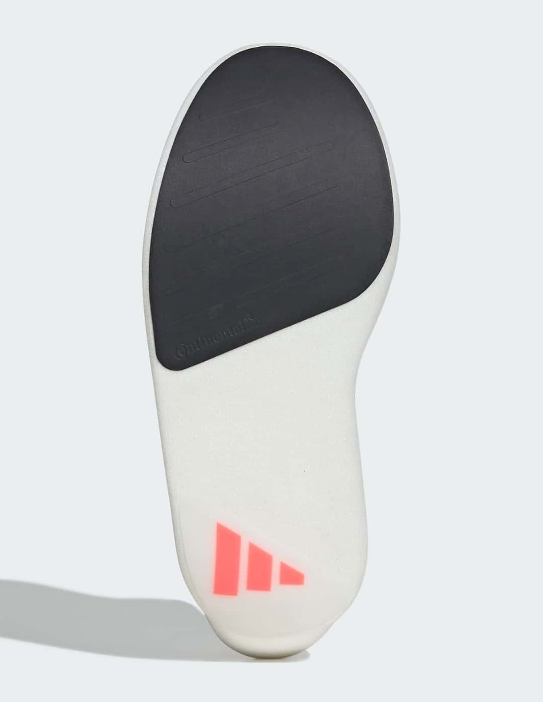 Suela de la adidas Adizero Adios Pro Evo 3 sobre fondo gris claro, con una pieza de goma negra en la parte delantera, el resto en espuma blanca y el logo de adidas en rojo en el talón