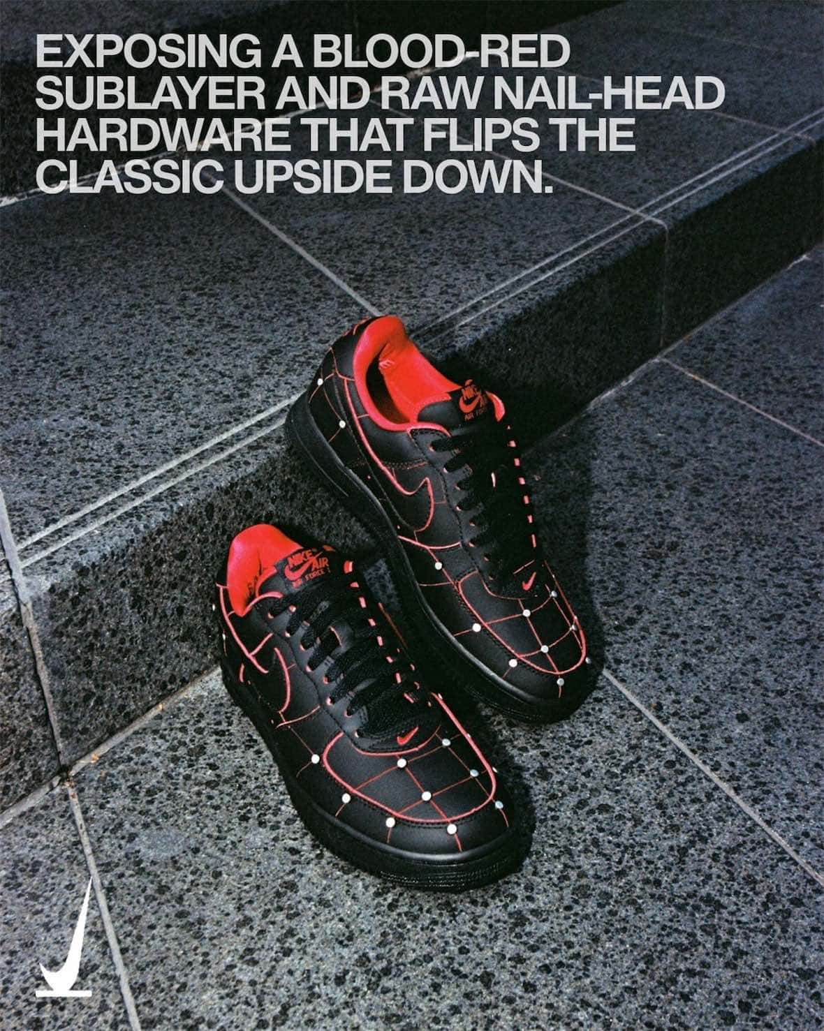 Par del Nike Air Force 1 '01 Nightmare apoyado en un escalón de piedra gris, en cuero negro con costuras rojas en cuadrícula, tachas plateadas en los cruces, forro rojo y logos Nike Air rojos en la lengüeta, con texto de campaña en inglés arriba