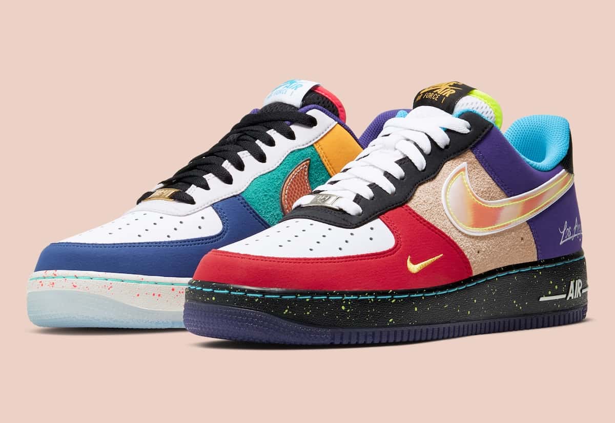 Par del Nike Air Force 1 Low What The LA en diagonal sobre fondo rosa claro: a la izquierda la zapatilla con puntera azul, gamuza verde, swoosh con textura de pelota de básquet y suela translúcida; a la derecha la de puntera roja, gamuza beige, swoosh iridiscente, talón violeta y mediasuela negra con salpicado verde flúor