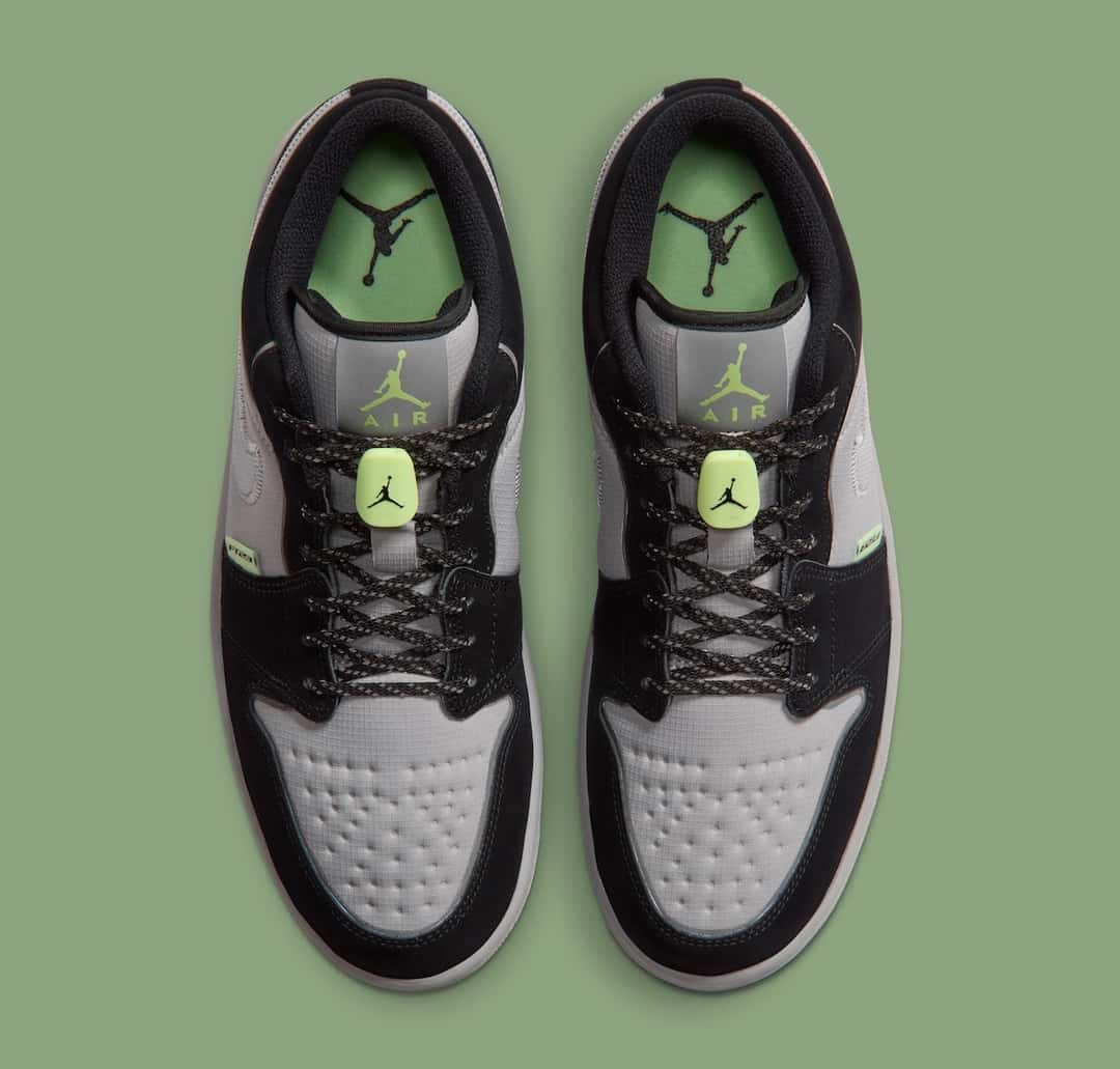 Vista superior del par de Air Jordan 1 Low Light Smoke Grey Barely Volt sobre fondo verde, con las plantillas verdes con el Jumpman, las trabas flúor y los cordones negros con puntos claros