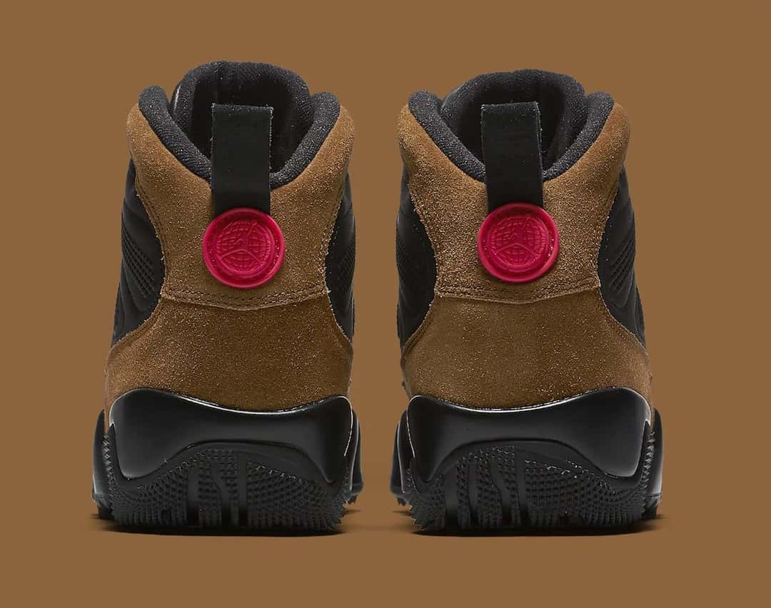 Talones del Air Jordan 9 Boot Olive sobre fondo marrón, con la gamuza verde oliva, el medallón rojo con el logo y la suela negra con tacos