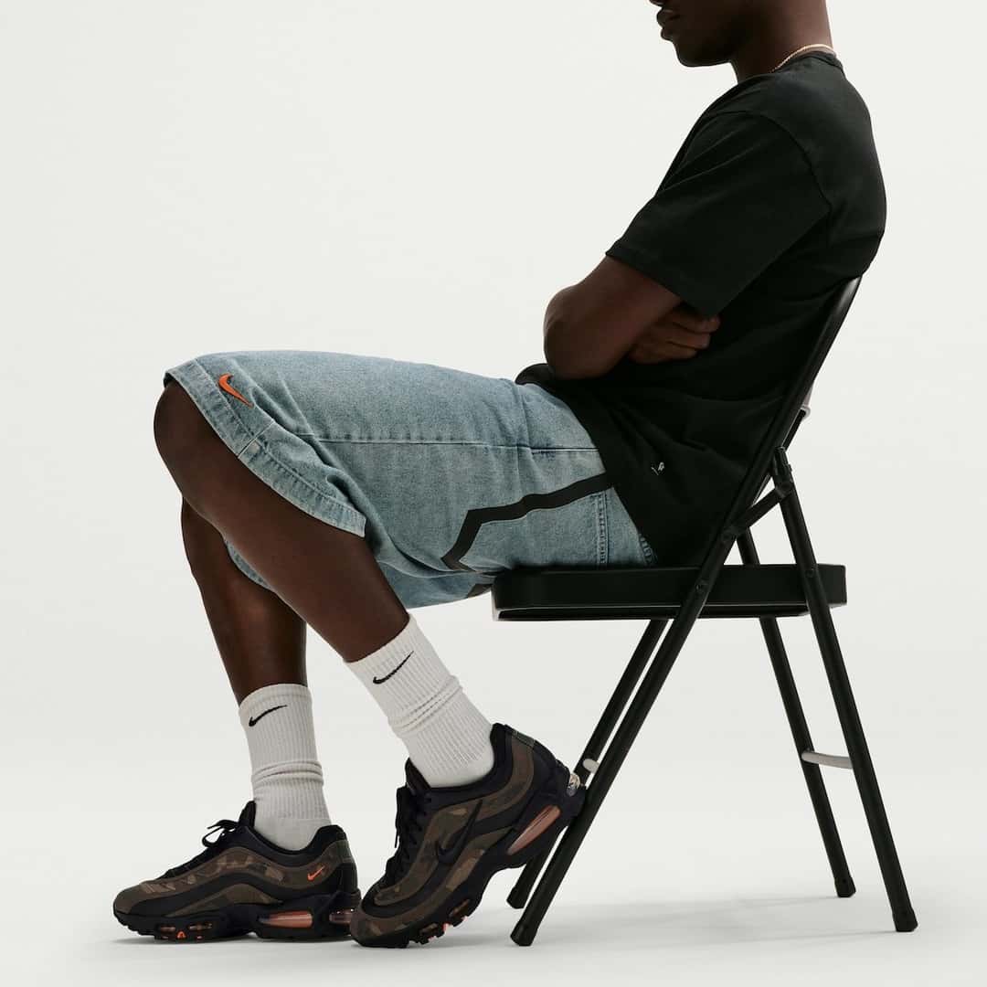 Persona sentada en una silla plegable con la Nike Air Max Joga Bonito Camo puesta, medias blancas y bermuda de jean