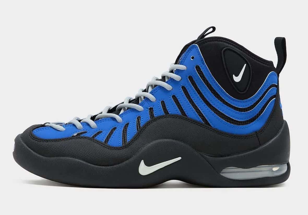 Nike Air Bakin Varsity Royal de perfil, con paneles azules sobre malla negra y Swoosh claro, sobre fondo gris claro
