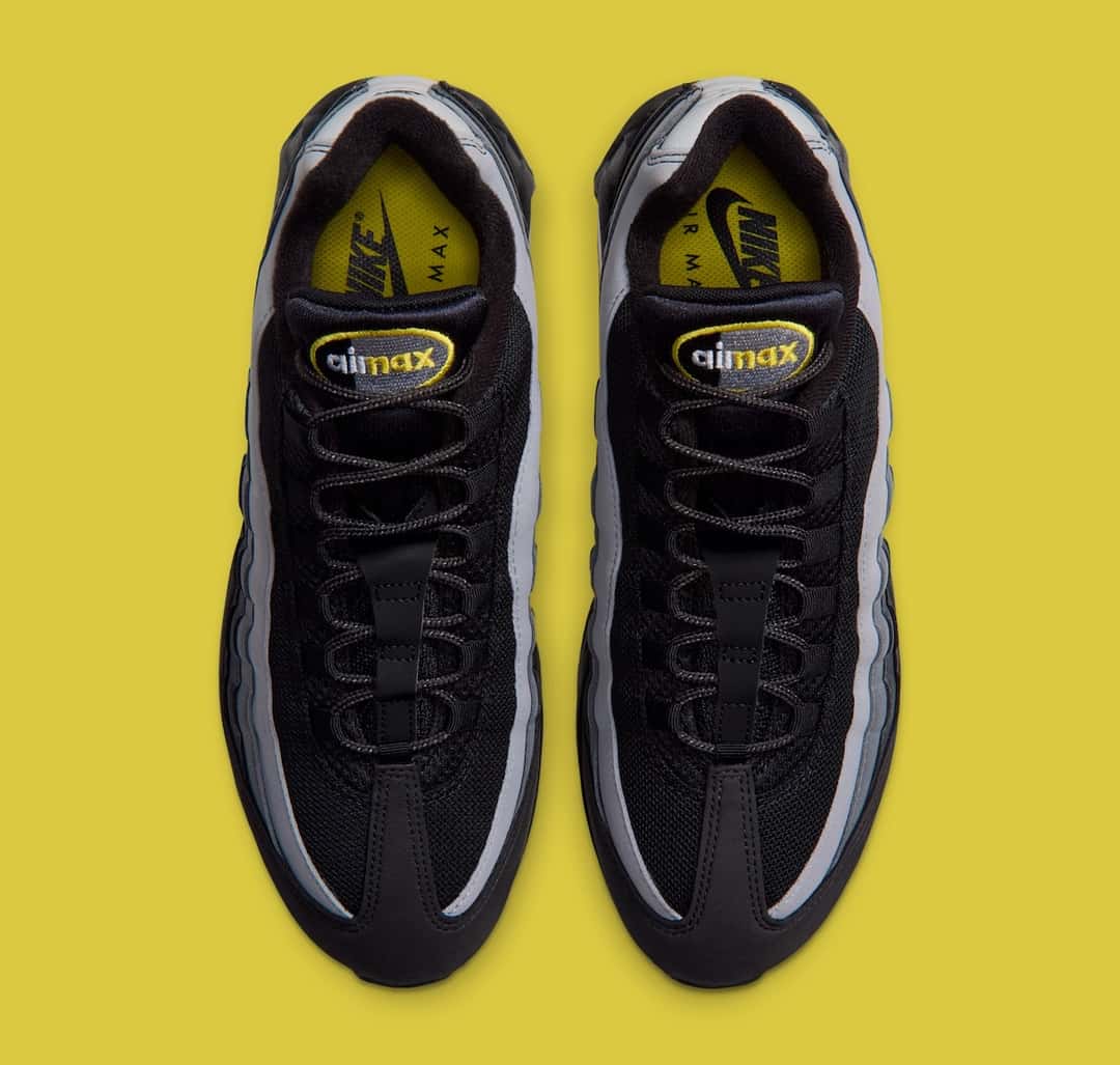 Par de Nike Air Max 95 del pack Batman visto desde arriba sobre fondo amarillo, con malla negra, laterales en degradé gris y la plantilla amarilla con el logo Air Max