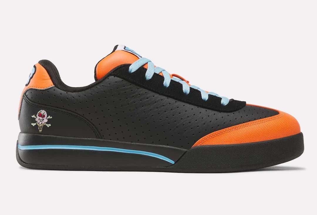 BBC ICECREAM x Reebok Board Flip Pumpkin de perfil sobre fondo gris claro, con cuero negro perforado, puntera y talón naranjas, cordones celestes, el helado con calavera bordado cerca del talón y una línea celeste en la suela negra