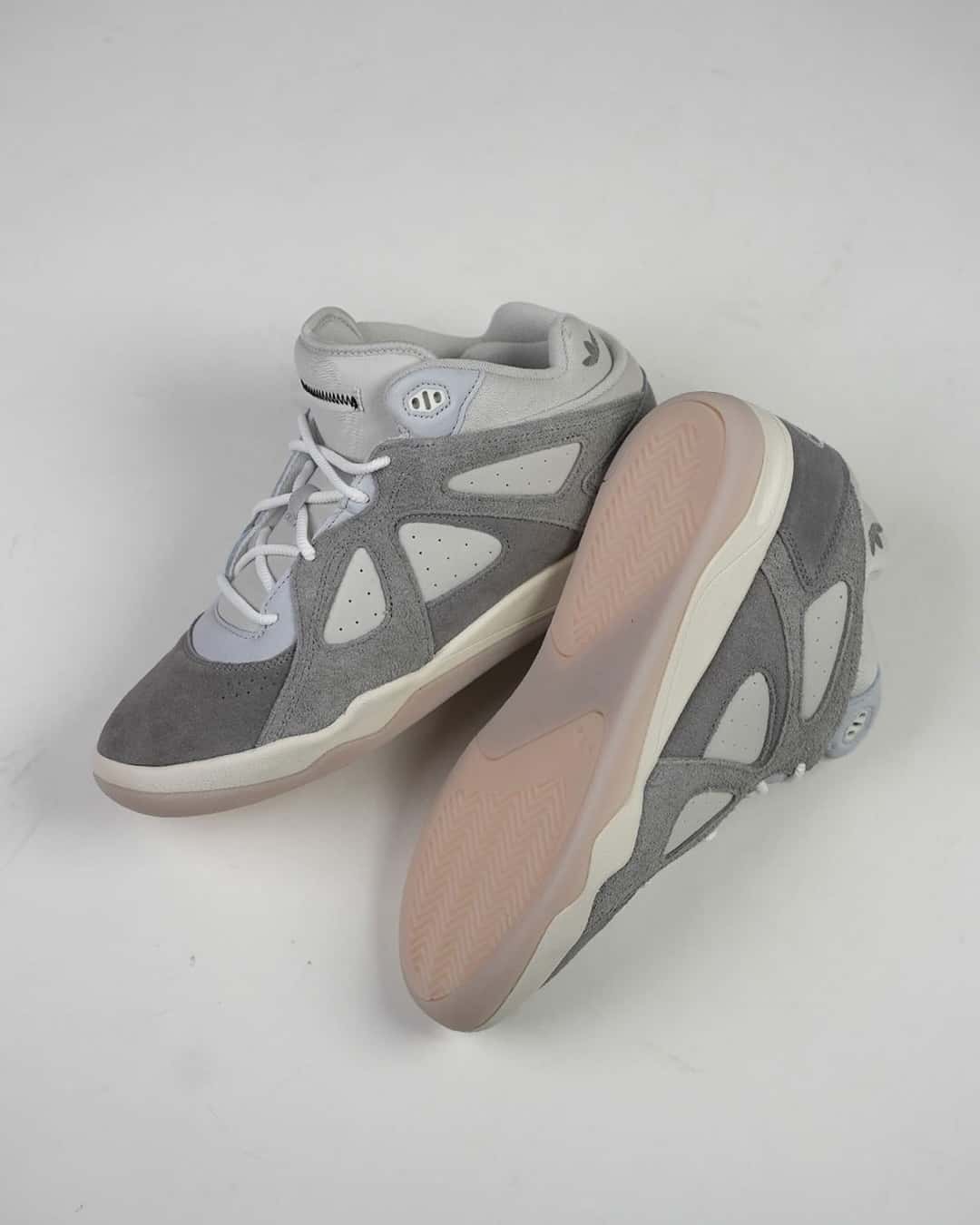 Par de la adidas BadBo 1.0 Grey Three apoyado sobre fondo gris claro, con la gamuza gris, los paneles de cuero claro y la suela translúcida