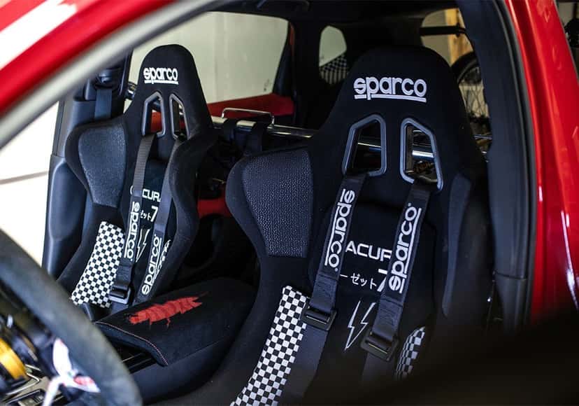 Butacas de competición Sparco negras dentro del Acura ADX CZ-77, con cinturones a cuadros y un rayo bordado