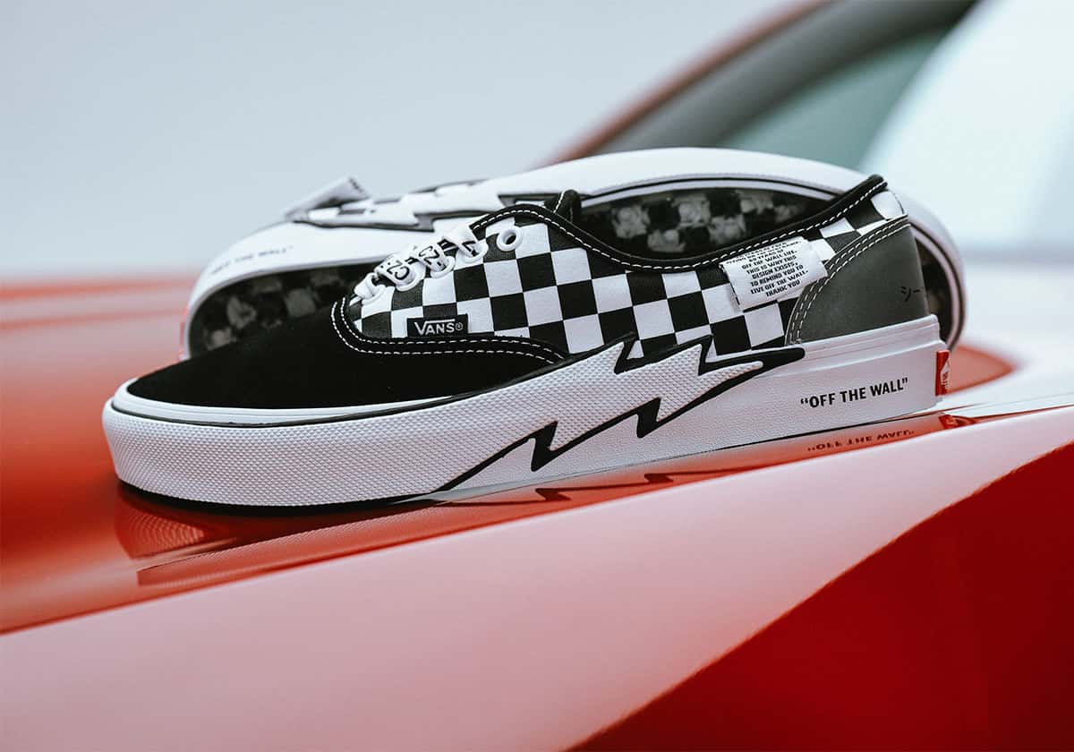 Vans Authentic de Coco Zurita a cuadros blancos y negros, con un rayo negro en el borde de goma, apoyada sobre el capó rojo de un auto