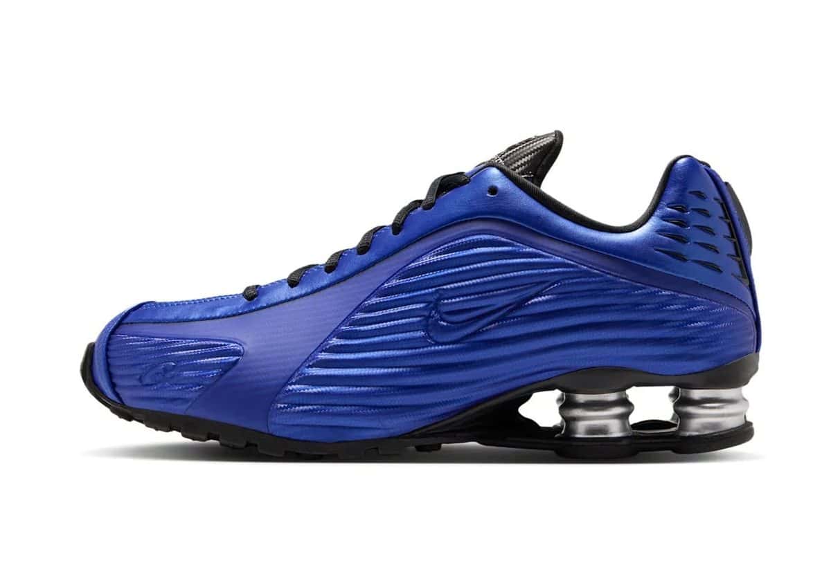 Corteiz x Nike Shox R419 Mystique azul Game Royal de perfil, con relieves horizontales en el costado, cordones negros y columnas Shox plateadas