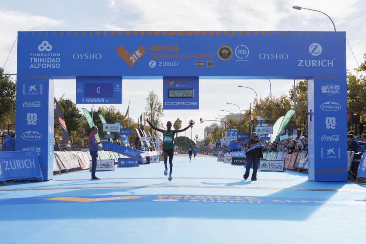 El ganador del Medio Maratón de Valencia 2026 levanta los brazos al cruzar la meta, con 0:58:03 en el reloj del arco de llegada