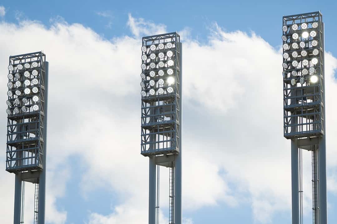 Foto de archivo: tres torres de iluminación de Progressive Field, el estadio de los Cleveland Guardians, con las luces encendidas contra un cielo celeste con nubes blancas
