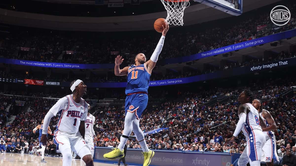 Jalen Brunson, con la camiseta azul número 11 de los Knicks, entra en bandeja ante jugadores de los 76ers vestidos de blanco en el Xfinity Mobile Arena de Philadelphia