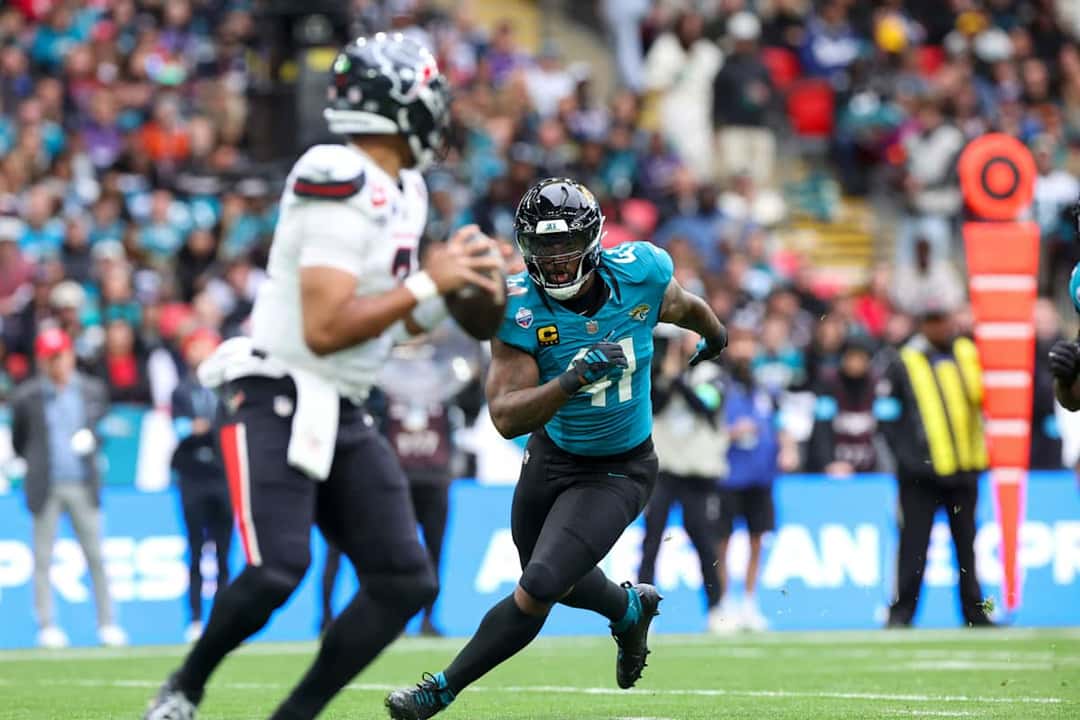 Un defensor de los Jaguars con la camiseta turquesa número 41 y la C de capitán corre hacia el quarterback de los Texans, de camiseta blanca, que prepara un pase en Wembley