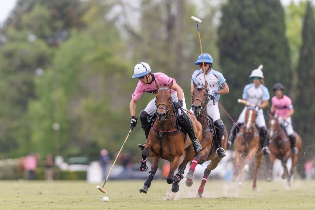 Un jugador de camiseta rosa de Ellerstina Indios Chapaleufú conduce la bocha con el taco, perseguido por un rival de camiseta celeste de La Zeta Kazak, en una cancha de césped del Tortugas Country Club