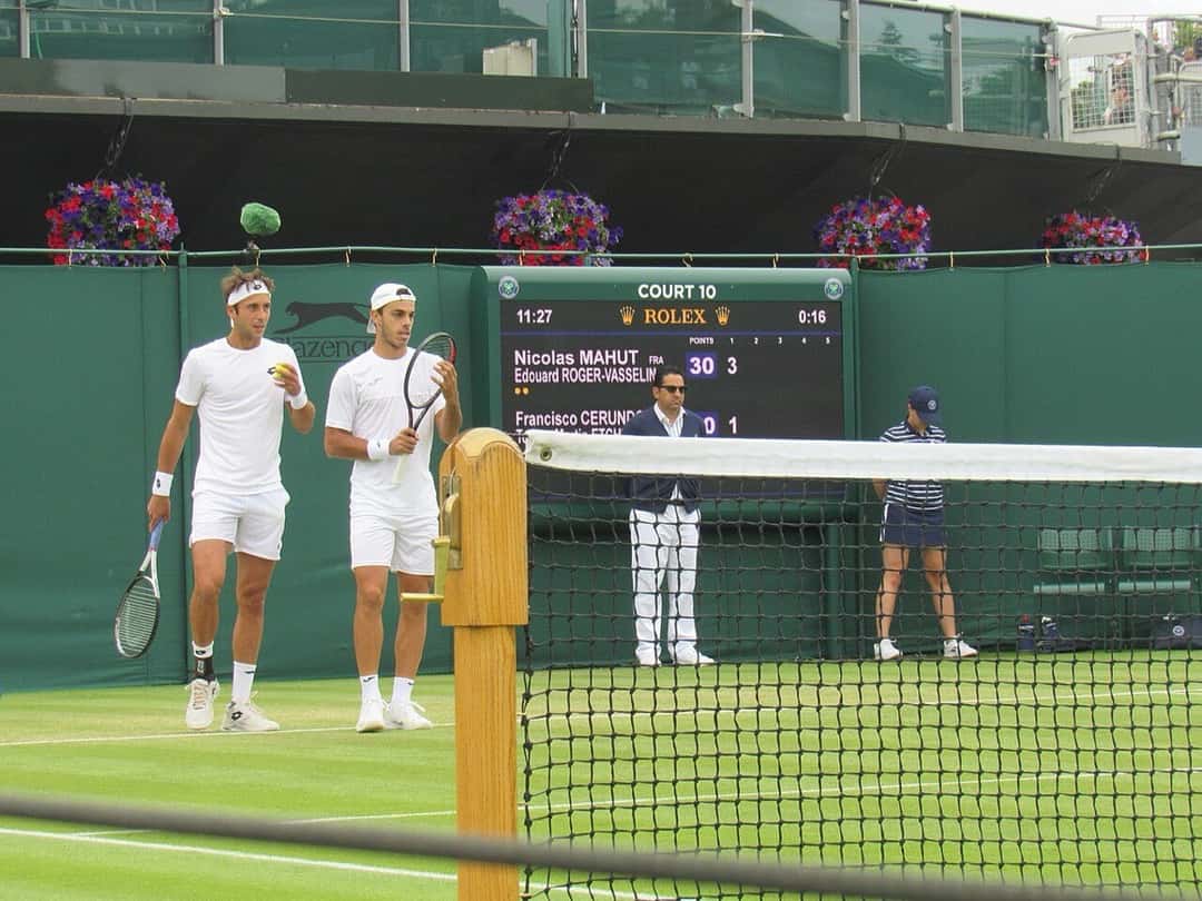 Foto de archivo: Francisco Cerúndolo y Tomás Martín Etcheverry, de blanco, entran a una cancha de Wimbledon para jugar un partido de dobles, con el tablero detrás