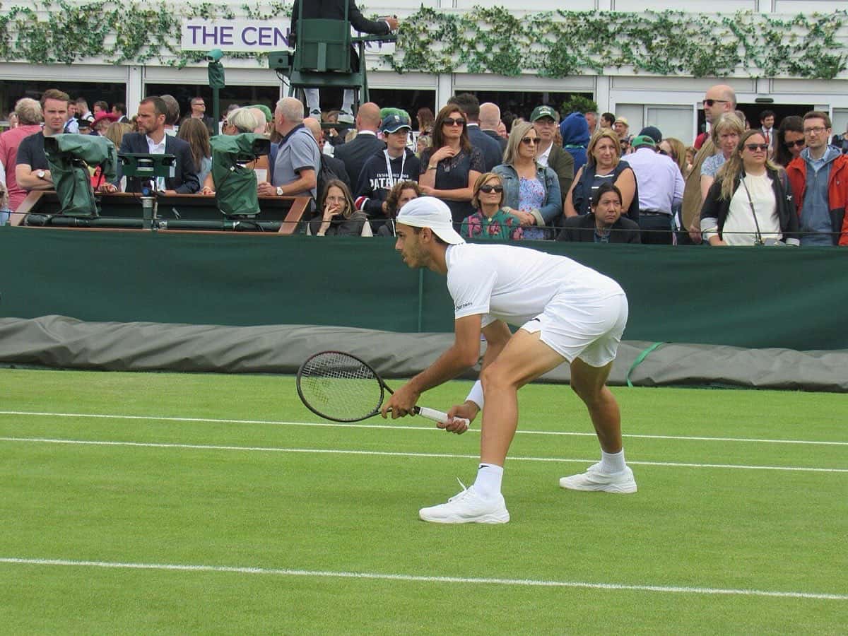 Foto de archivo: Francisco Cerúndolo, de blanco y con gorra hacia atrás, espera el saque en una cancha de césped de Wimbledon, con público detrás