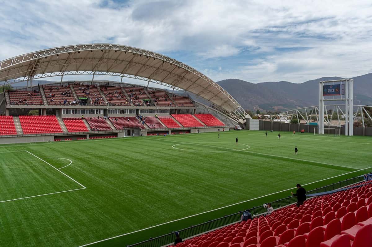 El estadio Municipal Nicolás Chahuán Nazar, de La Calera, con sus butacas rojas, el techo curvo de la tribuna y las montañas de fondo; foto de archivo de marzo de 2022 (foto: Carlos Figueroa Rojas, Wikimedia Commons, licencia CC BY-SA 4.0)